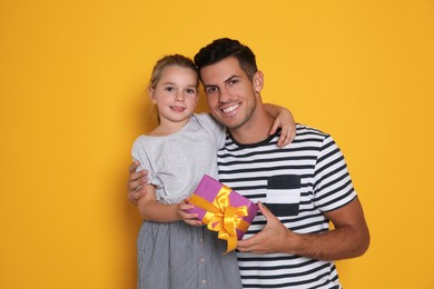 Photo of Man receiving gift for Father's Day from his daughter on yellow background