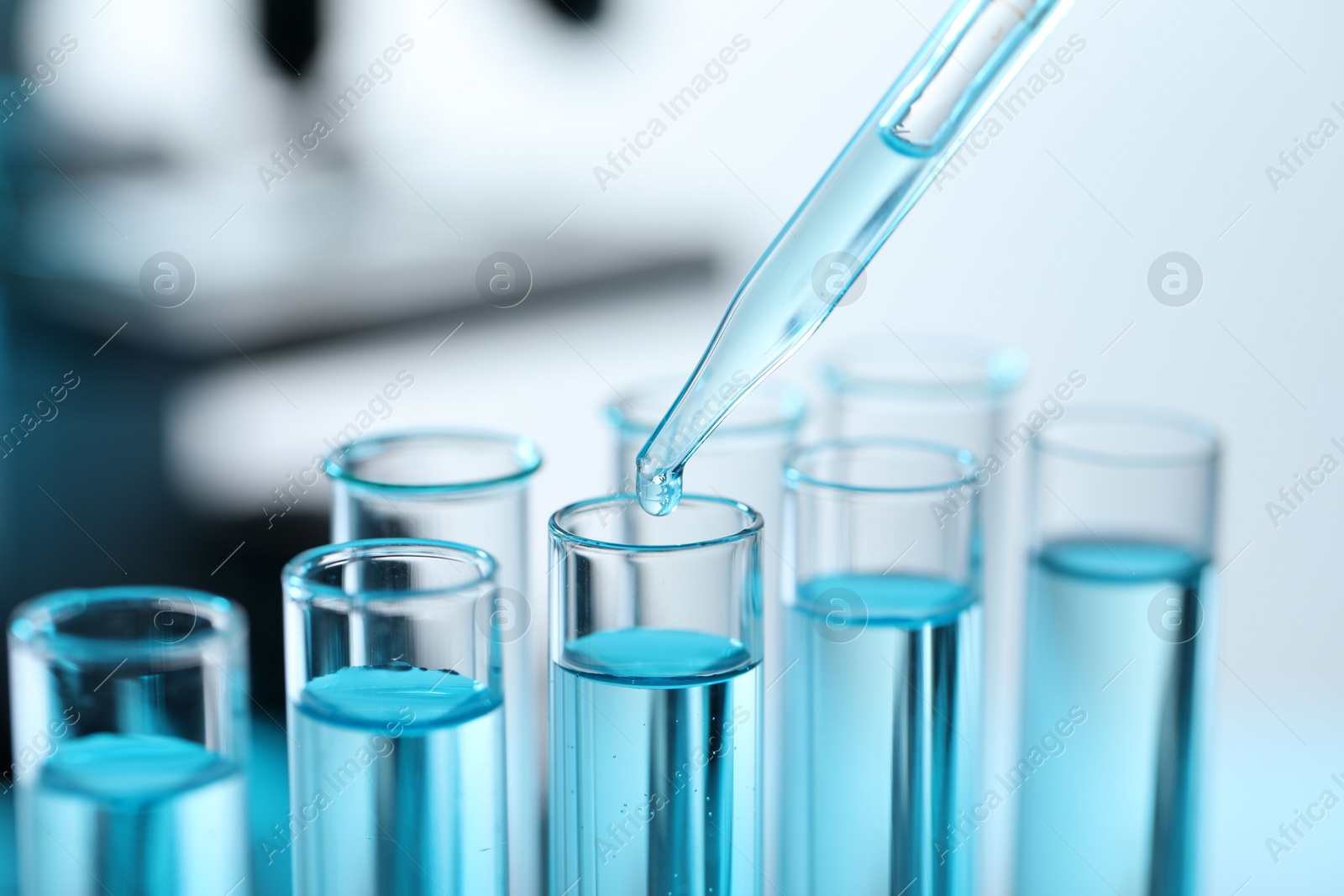 Photo of Dripping liquid from pipette into test tube on blurred background, closeup