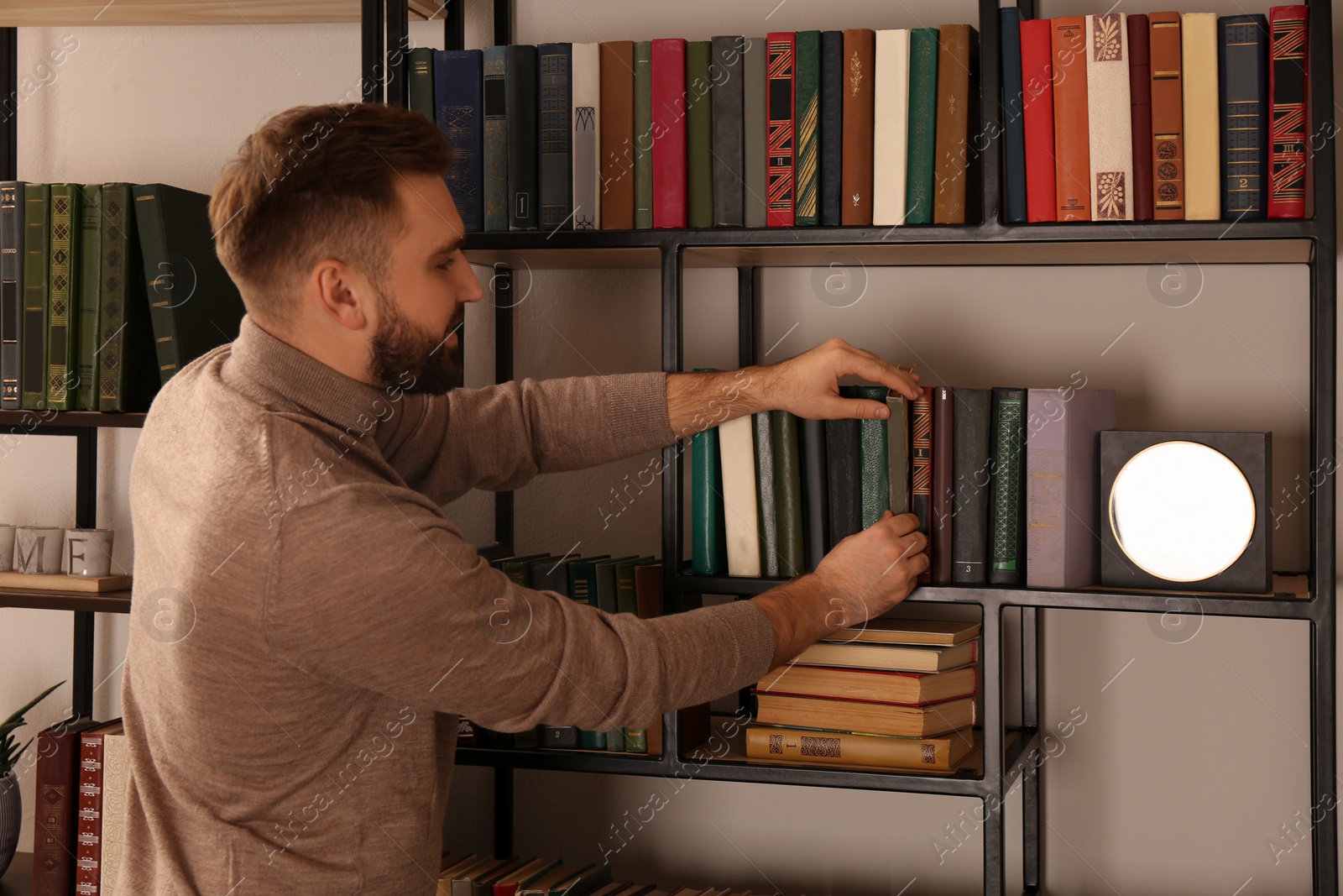 Photo of Young man choosing book on shelf in home library