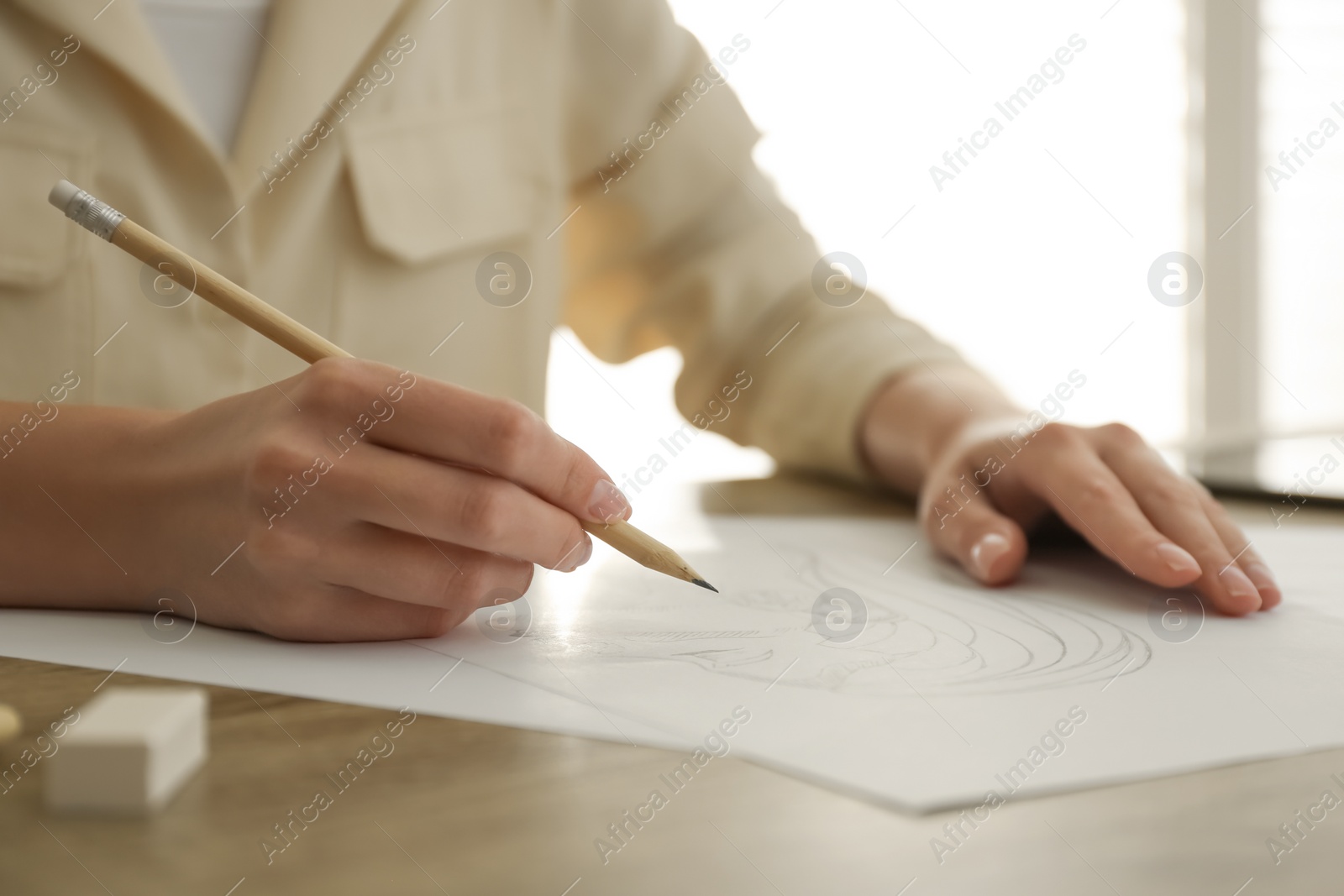 Photo of Woman drawing girl's portrait with pencil on sheet of paper at wooden table, closeup