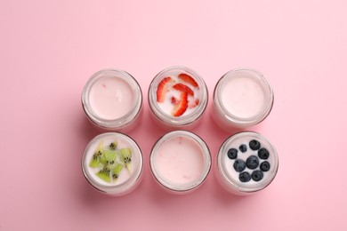 Tasty yogurt in glass jars and ingredients on pink background, flat lay