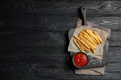 Photo of Delicious fresh french fries and tomato sauce on black wooden table, top view. Space for text