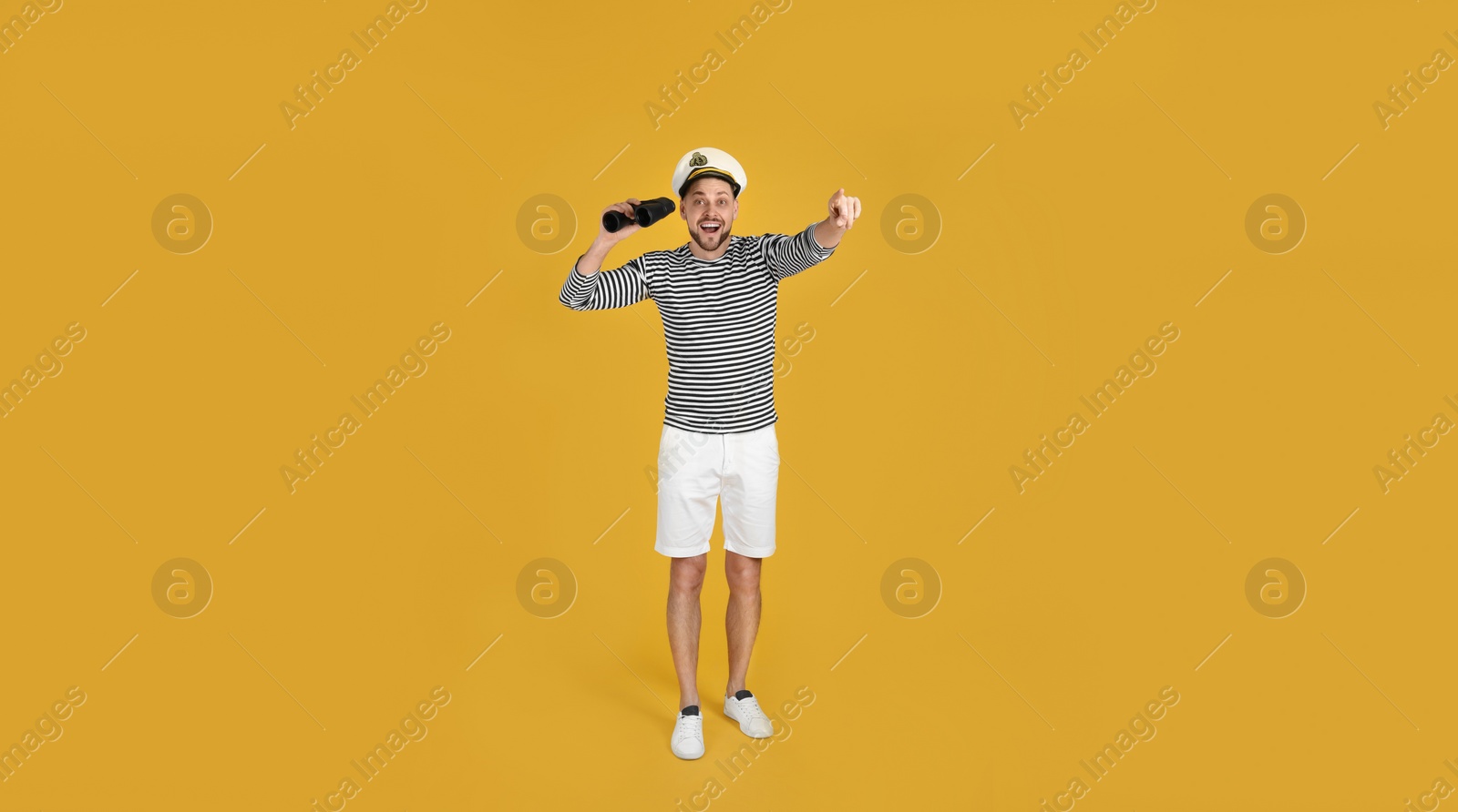 Photo of Excited sailor man with binoculars pointing on yellow background