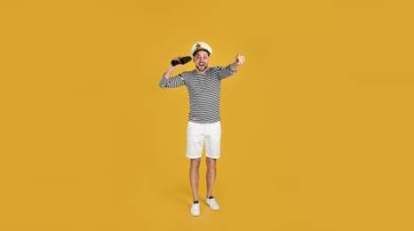 Photo of Excited sailor man with binoculars pointing on yellow background