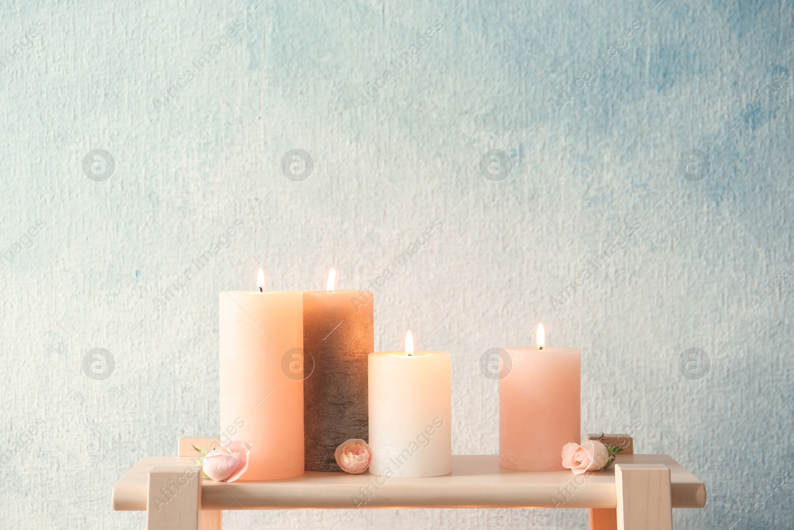 Photo of Candles with floral decor on table against color background