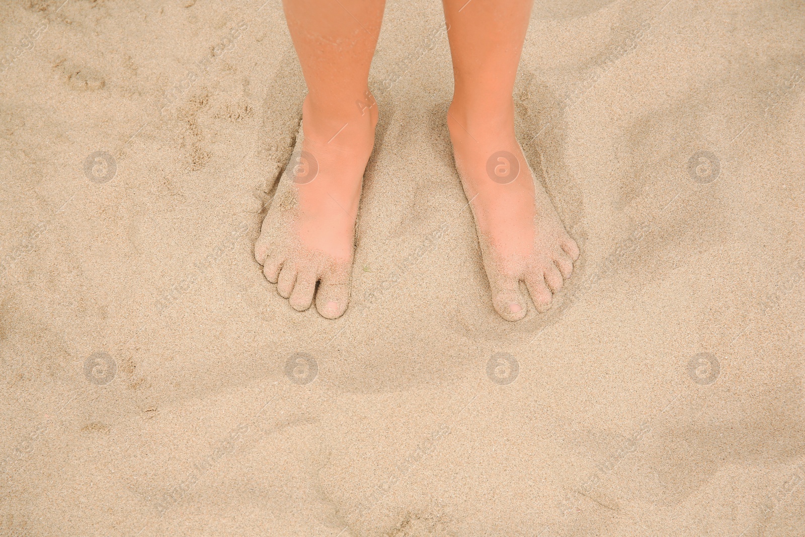 Photo of Little girl standing on sandy beach, closeup. Space for text