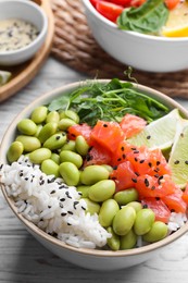 Photo of Delicious poke bowl with lime, fish and edamame beans on white wooden table, closeup