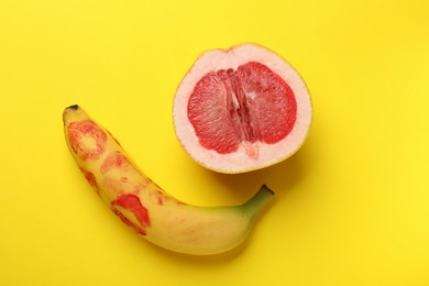 Photo of Banana with red lipstick marks and half of grapefruit on yellow background, flat lay. Sex concept