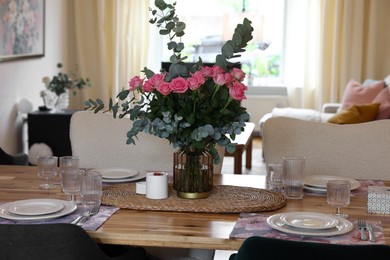 Beautiful table setting with bouquet of roses, napkins and candles in room