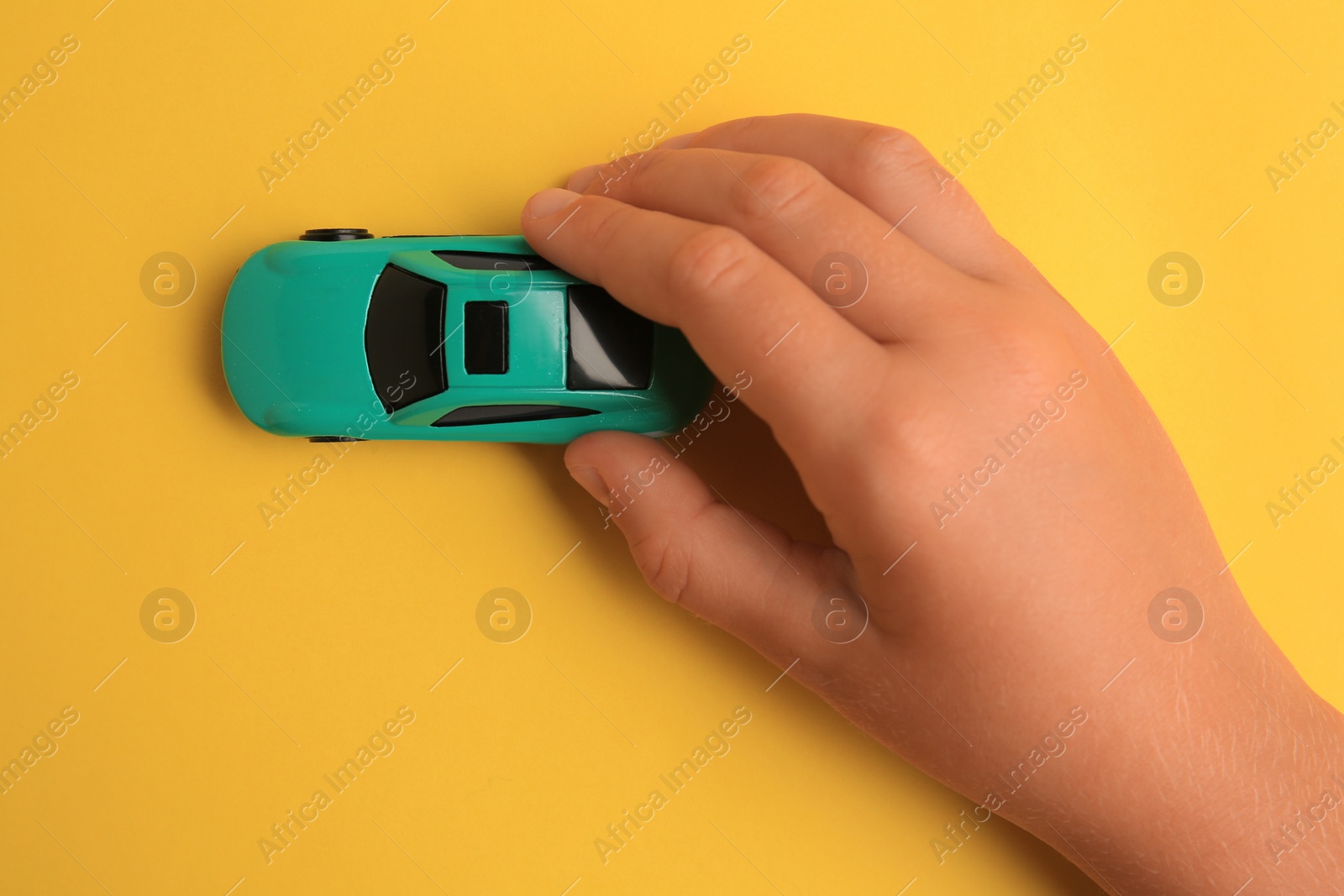 Photo of Child playing with toy car on yellow background, top view