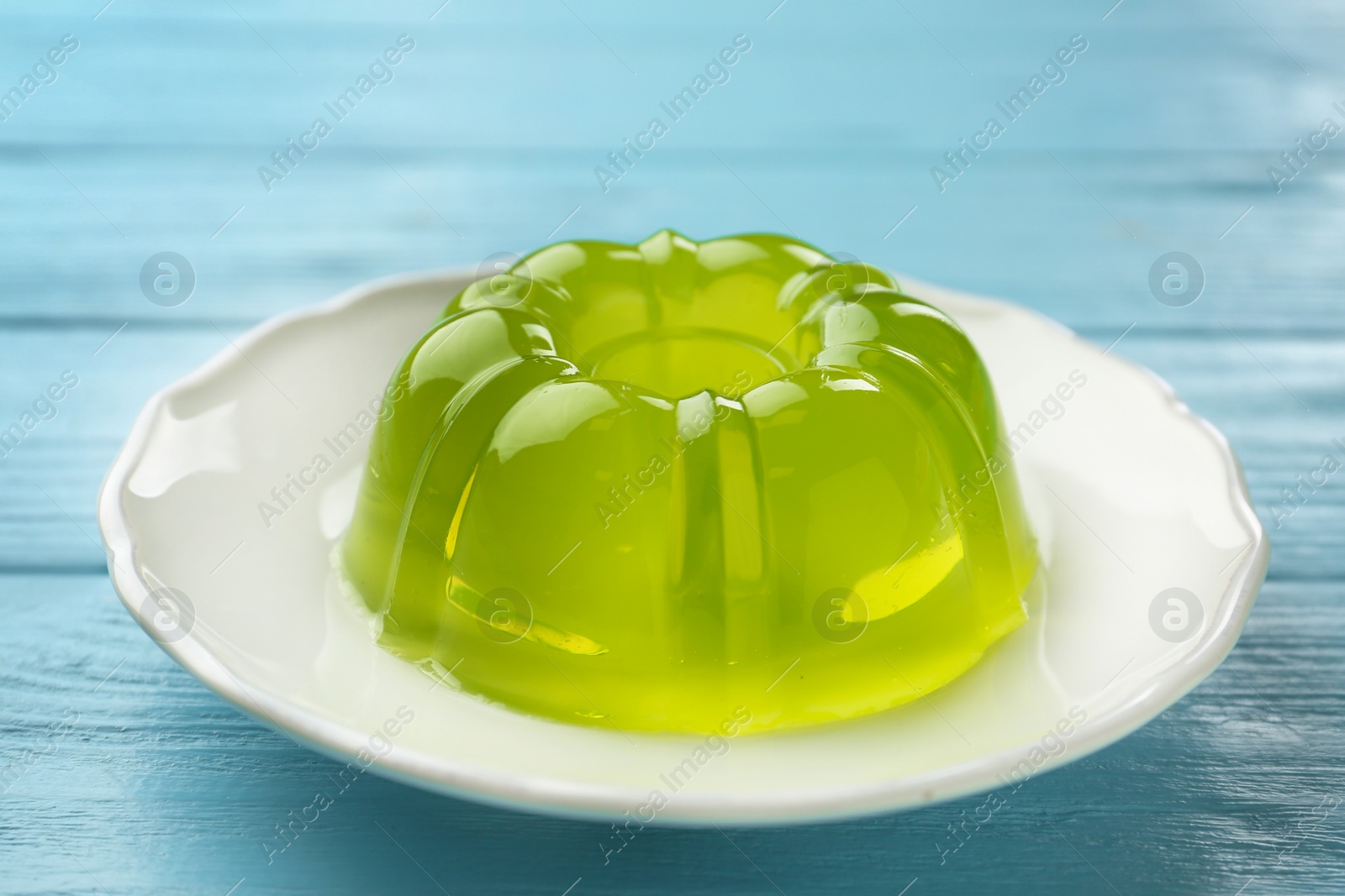 Photo of Plate of tasty fruit jelly on blue wooden table, closeup