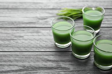 Photo of Glasses of wheat grass juice on wooden table. Space for text