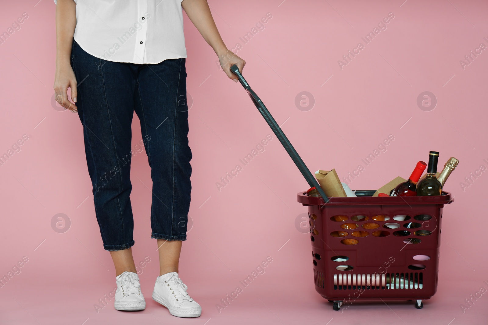 Photo of Woman with shopping basket full of different products on pink background, closeup