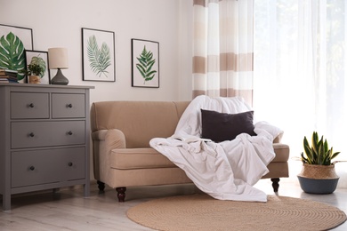 Comfortable sofa with blanket in stylish room