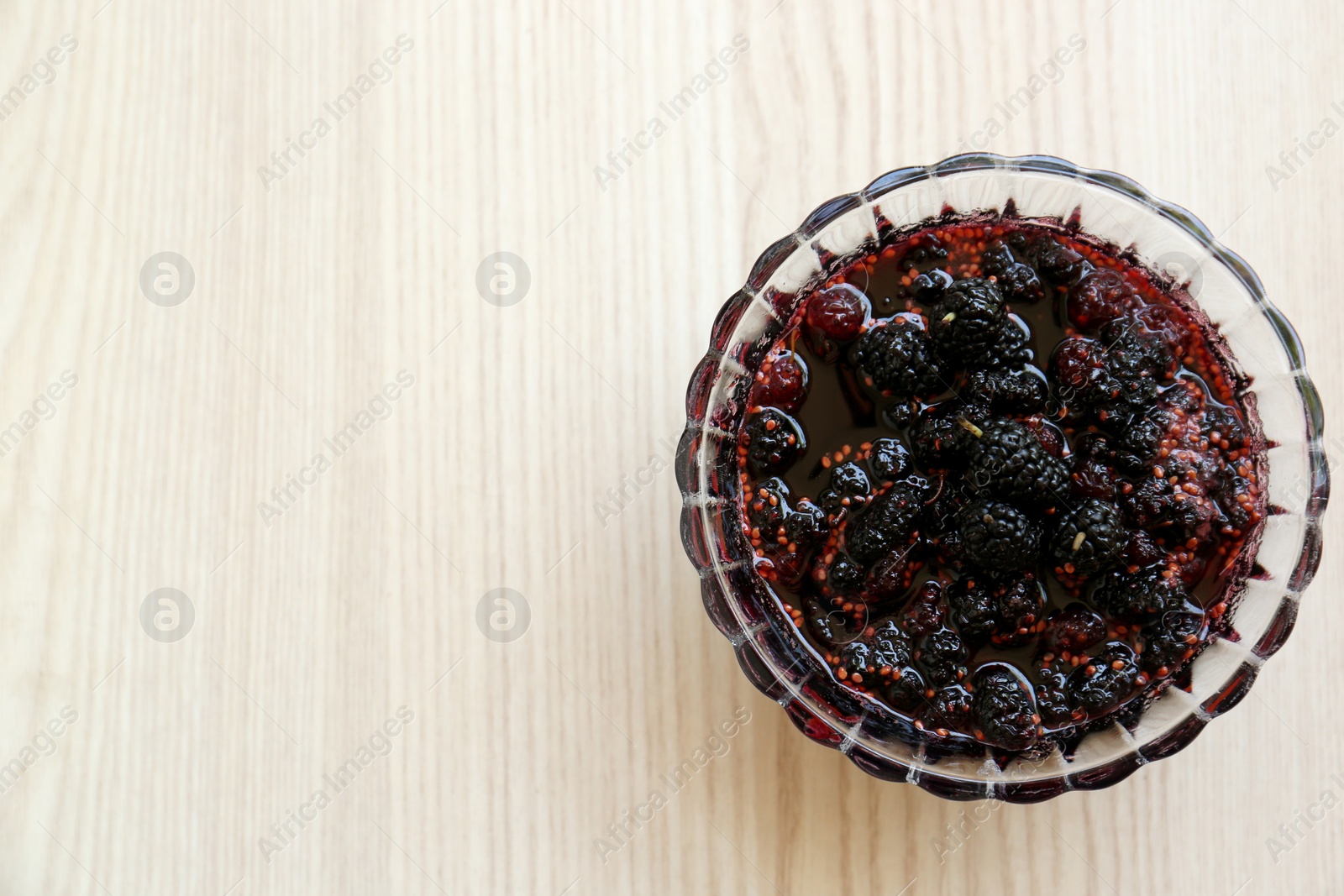 Photo of Bowl of sweet black mulberry jam on wooden table, top view. Space for text