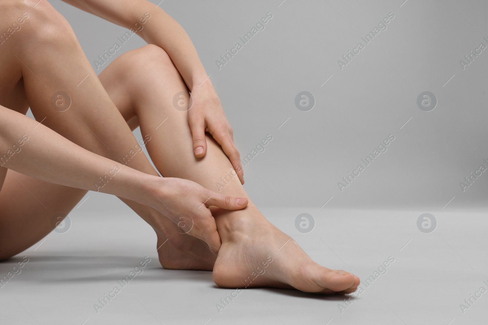 Photo of Woman suffering from leg pain on grey background, closeup. Space for text