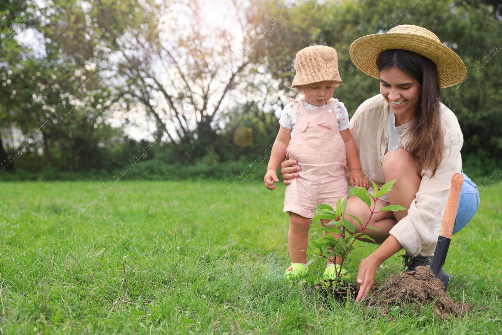 Photo of Mother and her baby daughter planting tree together in garden, space for text