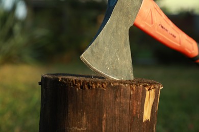 Photo of Metal axe in wooden log outdoors, closeup