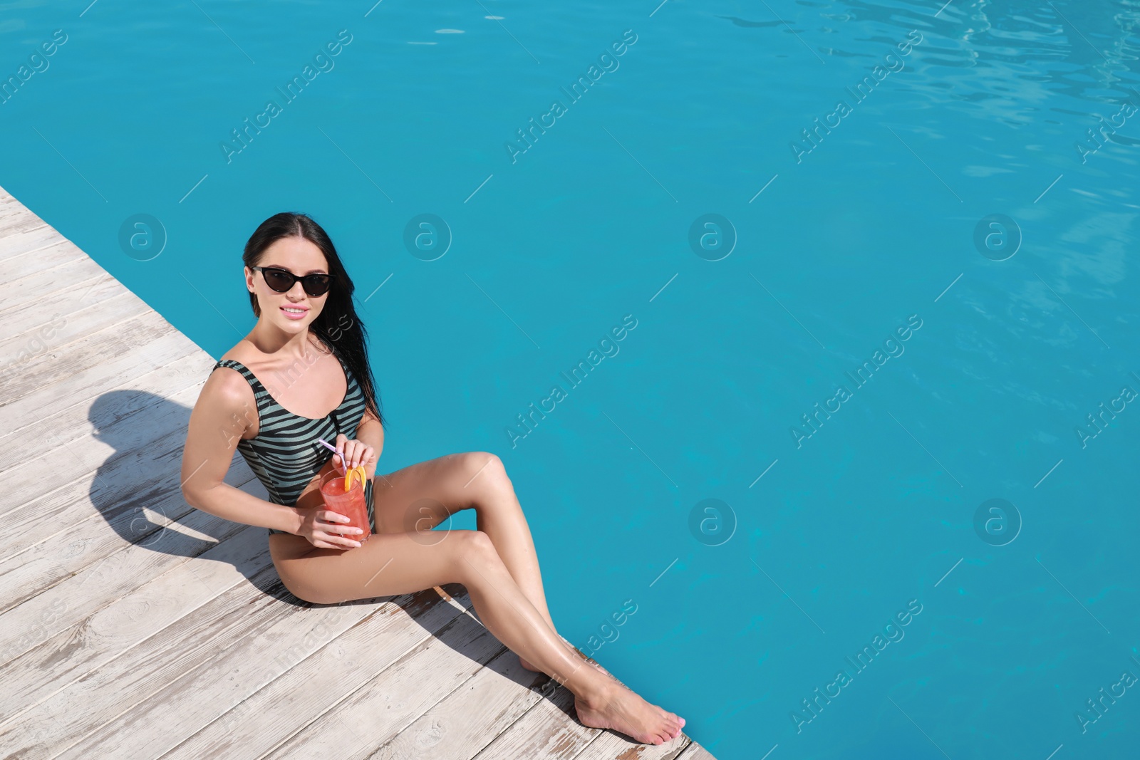 Photo of Beautiful young woman with refreshing cocktail near swimming pool on sunny day, above view