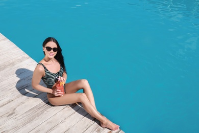 Photo of Beautiful young woman with refreshing cocktail near swimming pool on sunny day, above view