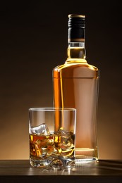 Whiskey with ice cubes in glass and bottle on wooden table