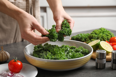 Photo of Woman cooking tasty kale salad on grey table, closeup