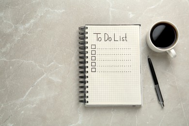 Notepad with unfilled To Do list, pen and cup of coffee on light grey marble table, flat lay. Space for text