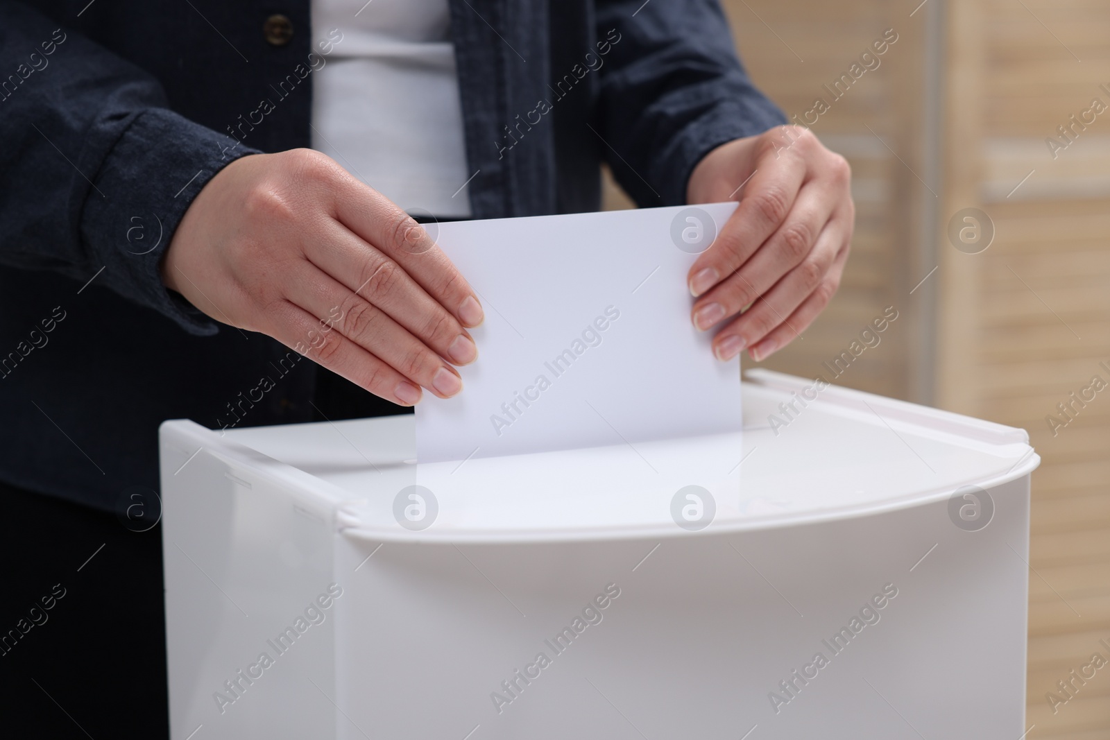 Photo of Woman putting her vote into ballot box on blurred background, closeup