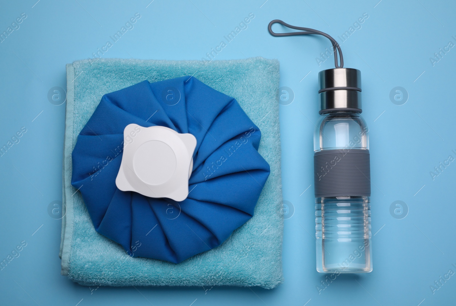 Photo of Bottle of water, cold compress and towel on light blue background, flat lay. Heat stroke treatment
