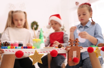 Cute little children making Christmas crafts at table in room, focus on festive decor