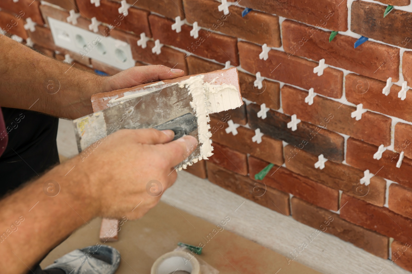 Photo of Professional builder applying cement onto decorative brick near wall, closeup. Tiles installation process