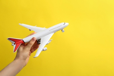 Woman holding toy airplane on yellow background, closeup. Space for text