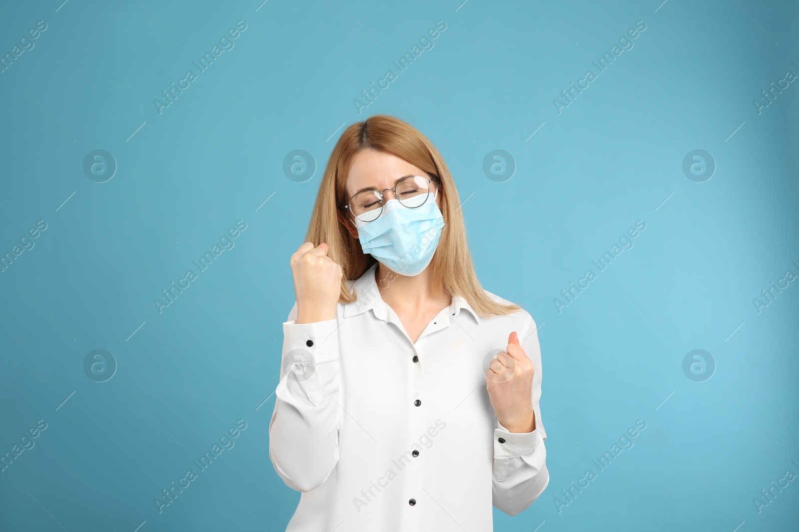 Photo of Emotional woman with protective mask on light blue background. Strong immunity concept
