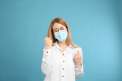 Photo of Emotional woman with protective mask on light blue background. Strong immunity concept