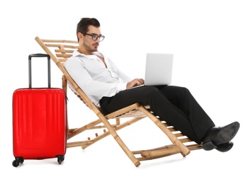 Young businessman with laptop and suitcase on sun lounger against white background. Beach accessories