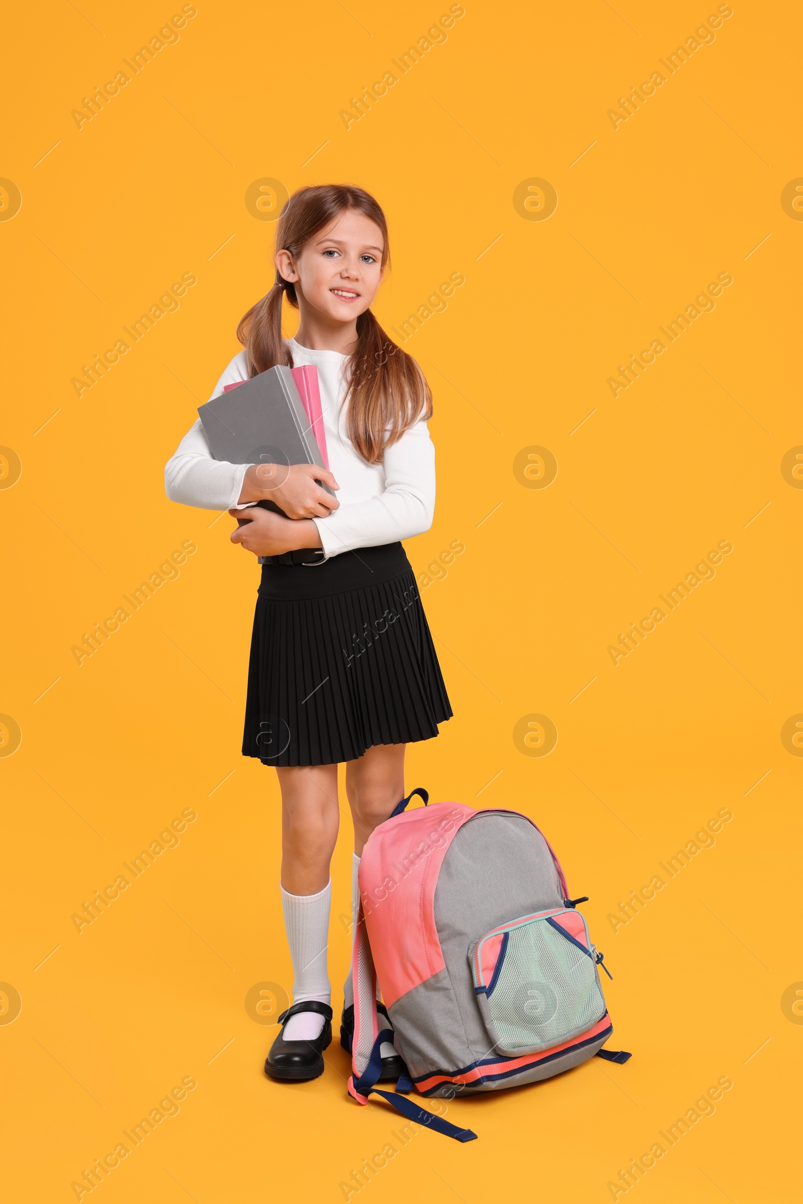 Photo of Happy schoolgirl with backpack and books on orange background