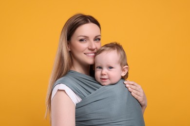 Photo of Mother holding her child in baby wrap on orange background