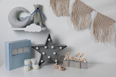 Album, baby shoes and toys on chest of drawers indoors. Children's room interior