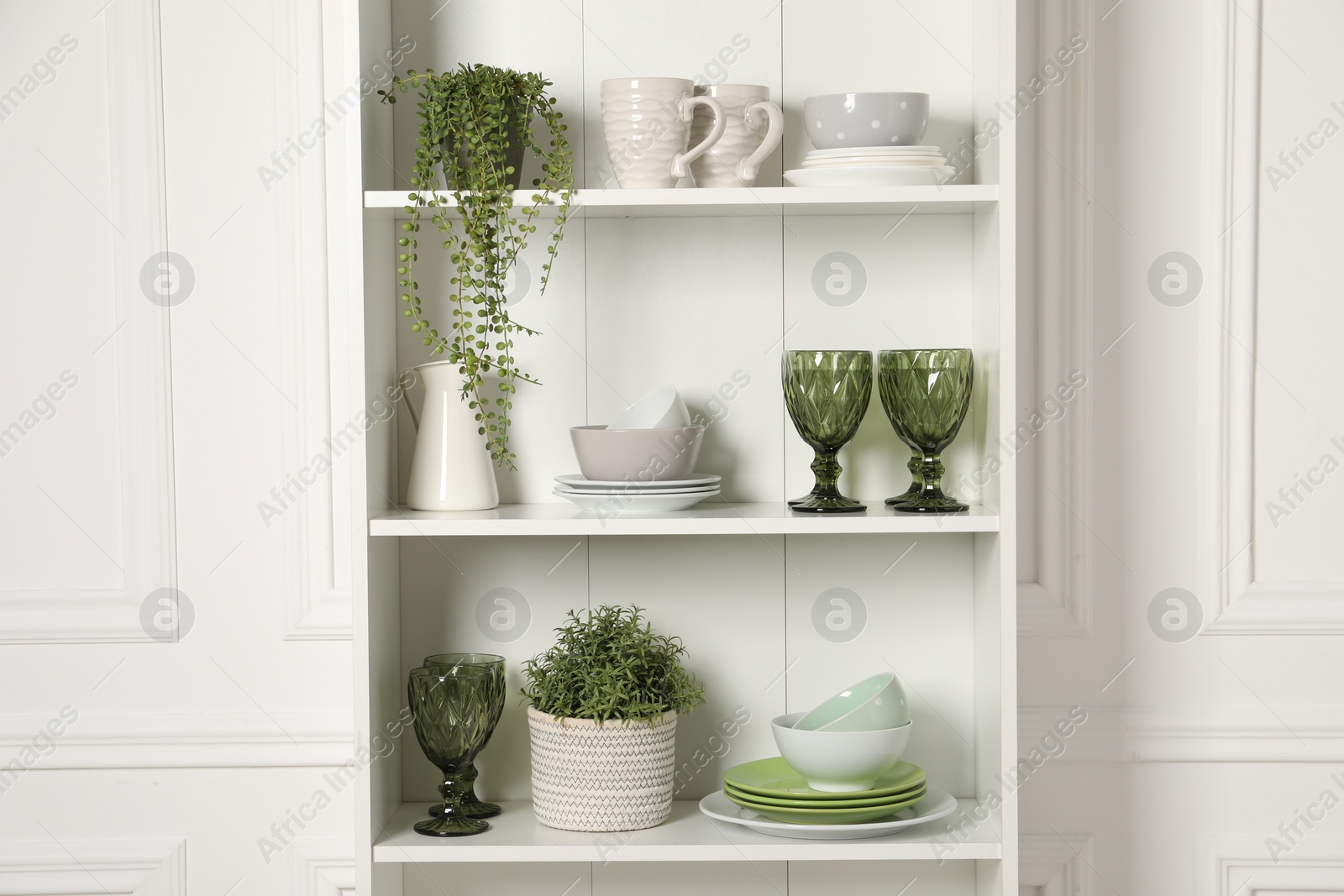 Photo of Different clean dishware and houseplants on shelves in cabinet indoors