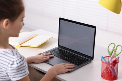 Photo of E-learning. Girl using laptop during online lesson at table indoors, closeup