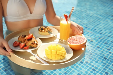 Young woman with delicious breakfast on floating tray in swimming pool, closeup