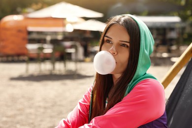 Photo of Beautiful young woman blowing chewing gum outdoors, space for text