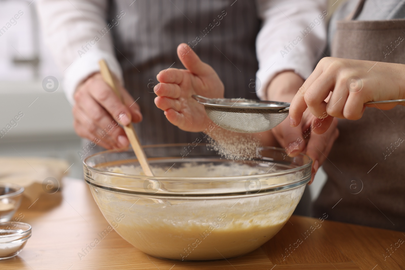 Photo of Making bread. Mother and her daughter preparing dough in bowl at wooden table in kitchen, closeup