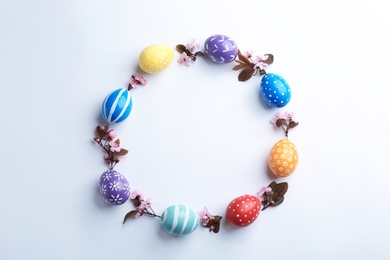 Photo of Frame made of painted Easter eggs and blossoming branches on white background, top view. Space for text