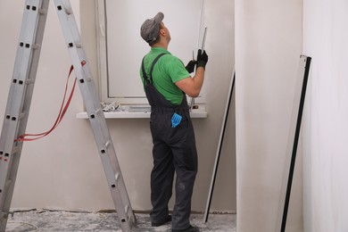 Worker in uniform installing double glazing window indoors, back view