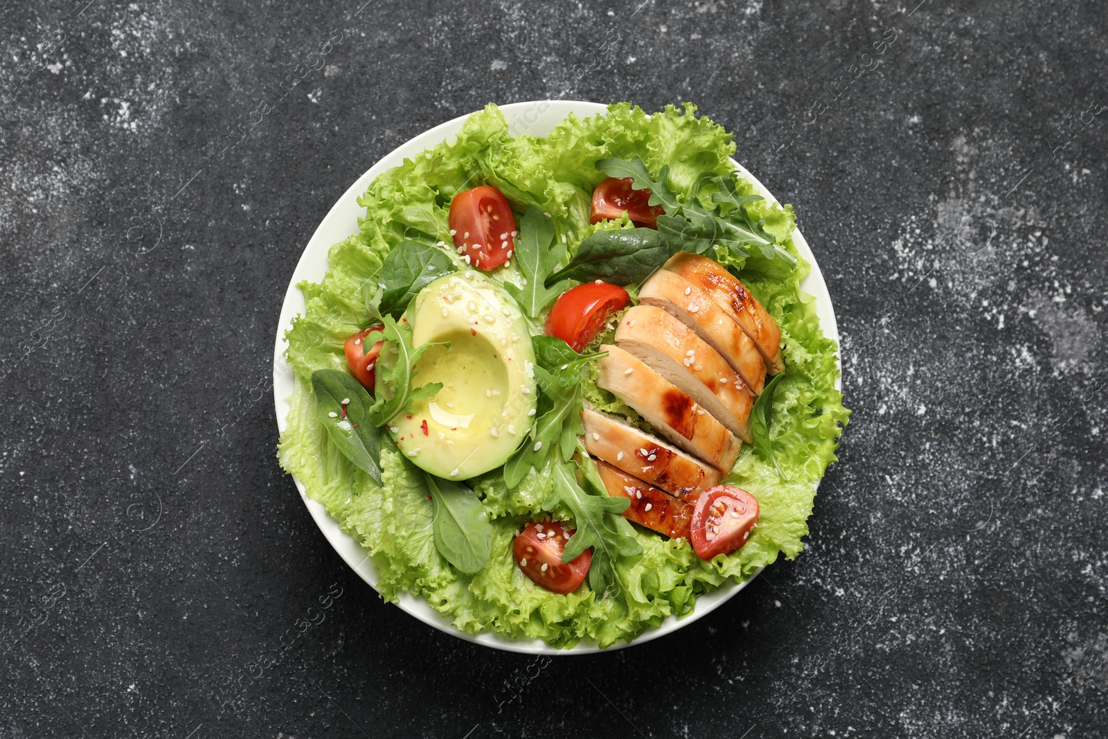 Photo of Delicious salad with chicken, cherry tomato and avocado on grey textured table, top view