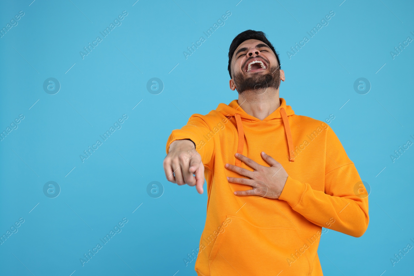 Photo of Handsome young man laughing while pointing at something on light blue background, space for text