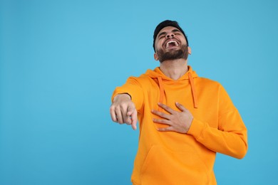 Handsome young man laughing while pointing at something on light blue background, space for text