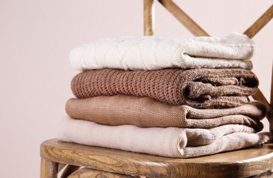 Stack of folded warm sweaters on wooden chair against light background