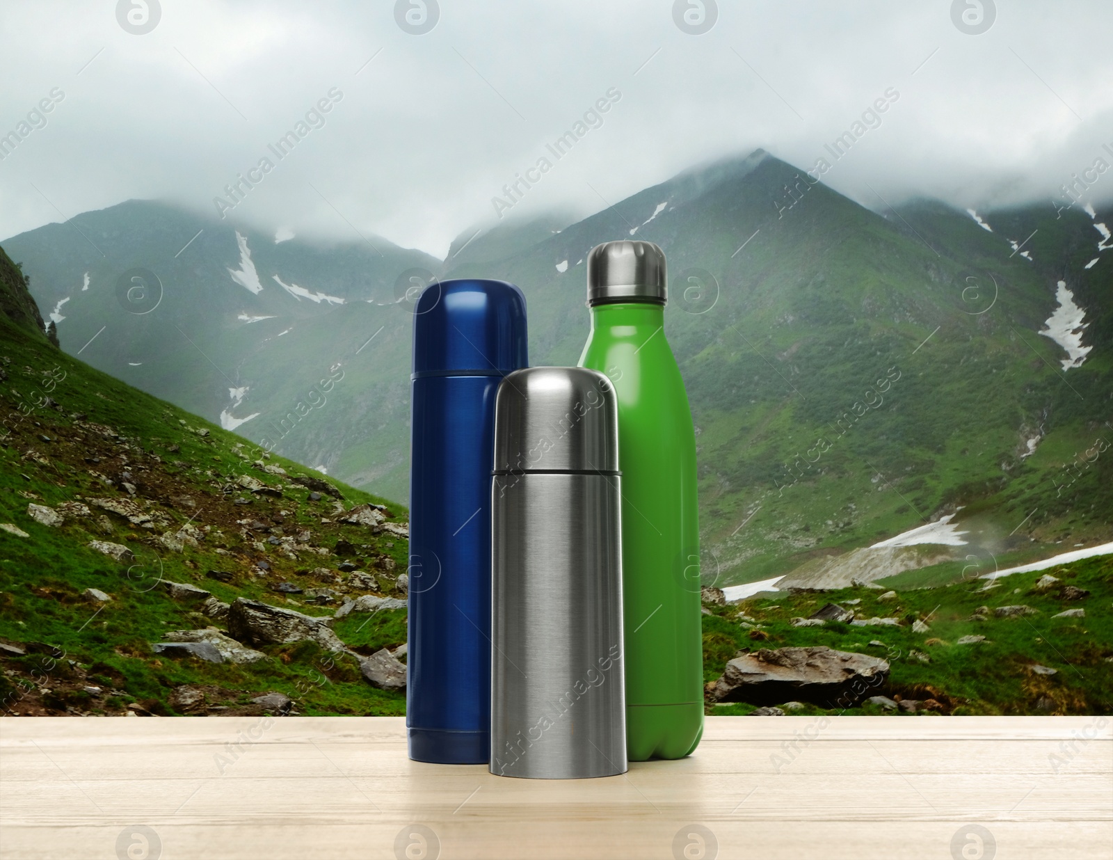 Image of Wooden desk with thermo bottles and mountain landscape on background